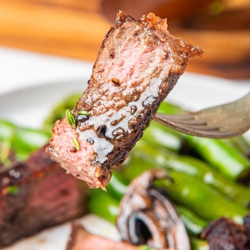 New York Strip Steak on a fork with green beans on a plate.