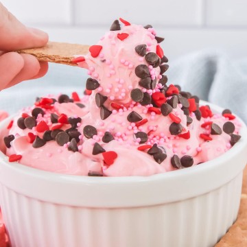 A person is scooping a pink dip out of a bowl.