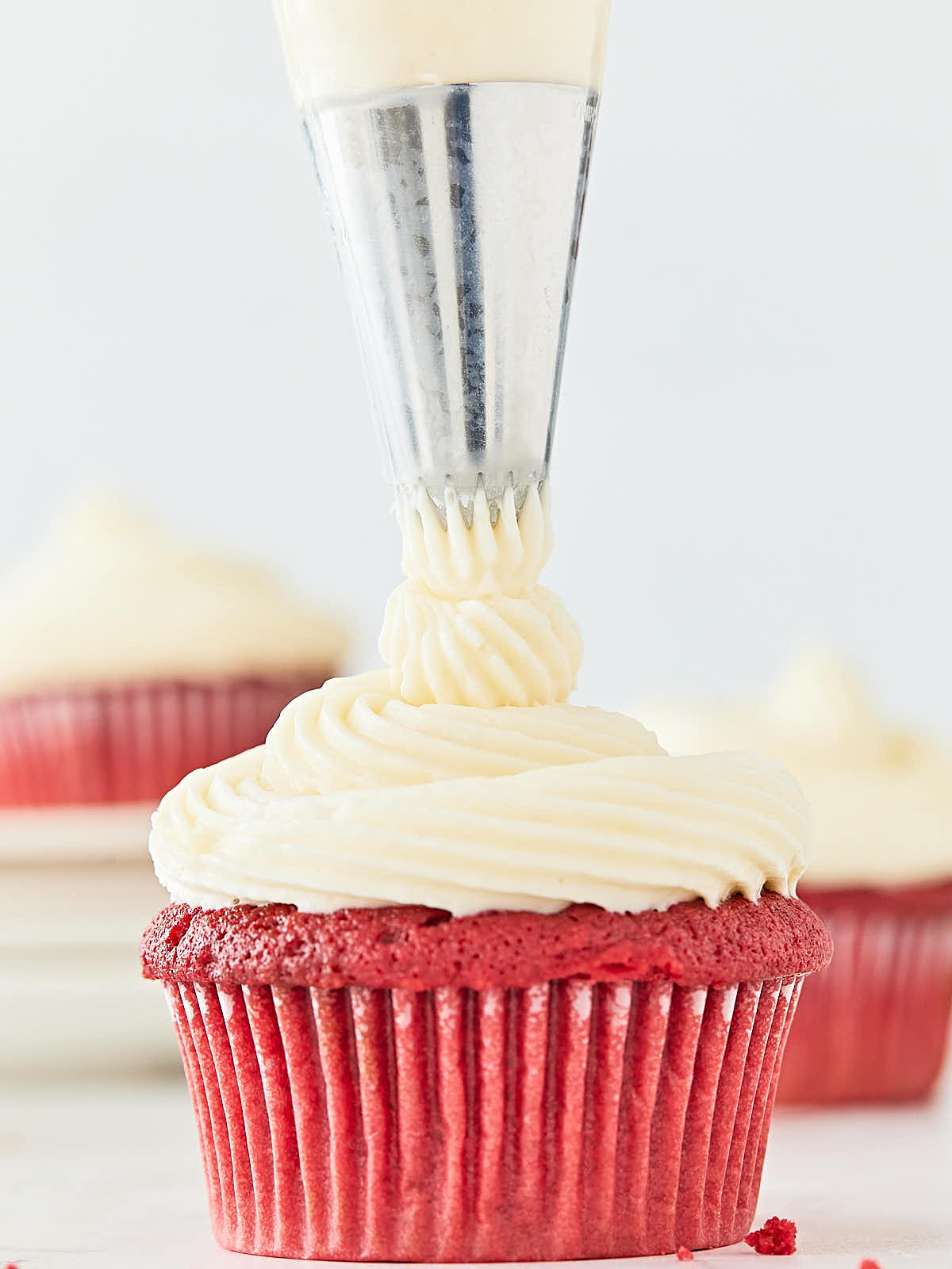 A red velvet cupcake being frosted with icing.