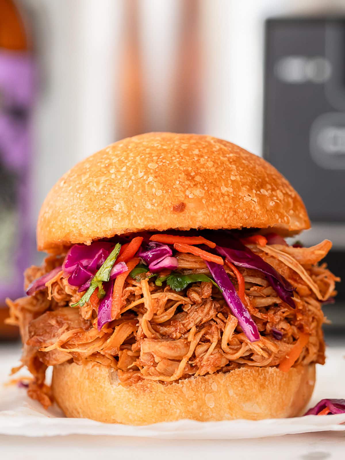 A slow cooker pulled chicken sandwich with slaw on a white plate.