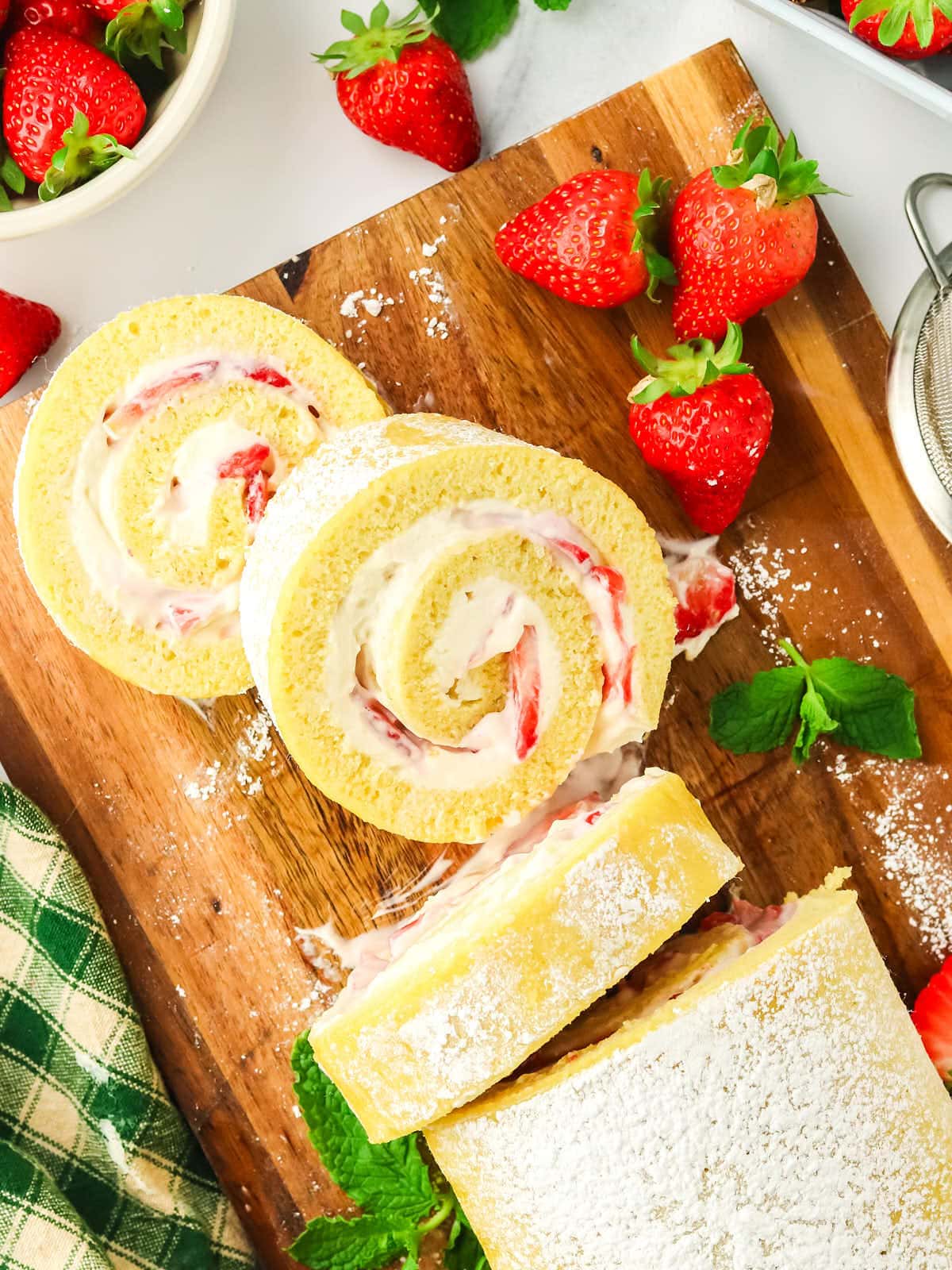 A strawberry roll with whipped cream and strawberries on a cutting board.