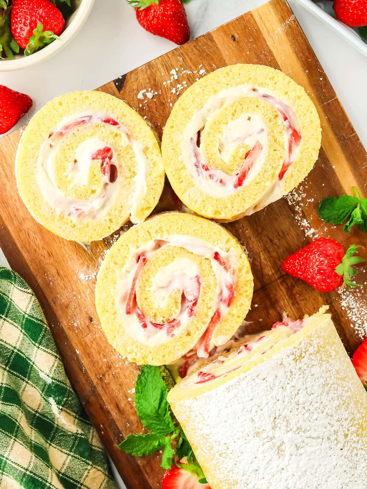 A strawberry roll with cream and strawberries on a cutting board.