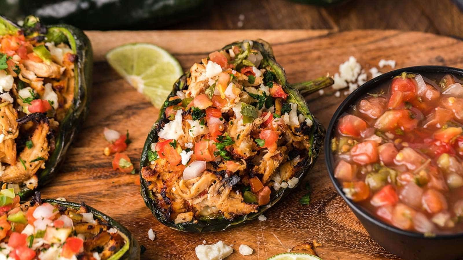 Stuffed jalapeos with guacamole and salsa on a wooden cutting board.