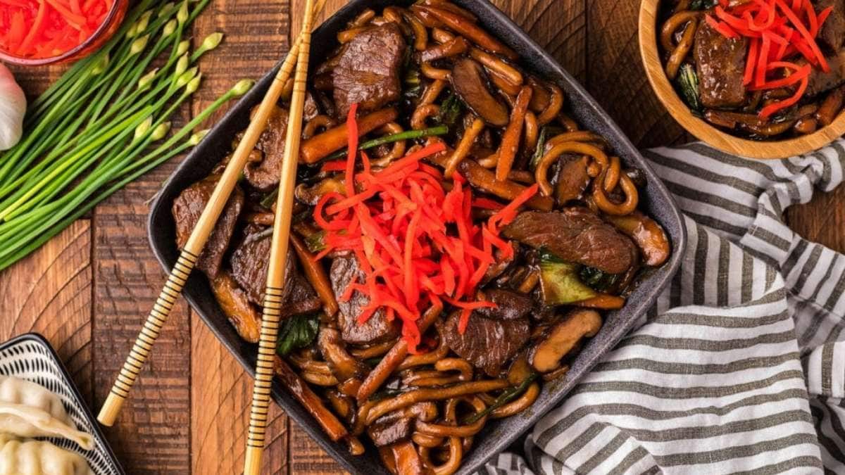 Chinese beef stir fry with vegetables and chopsticks on a wooden table.