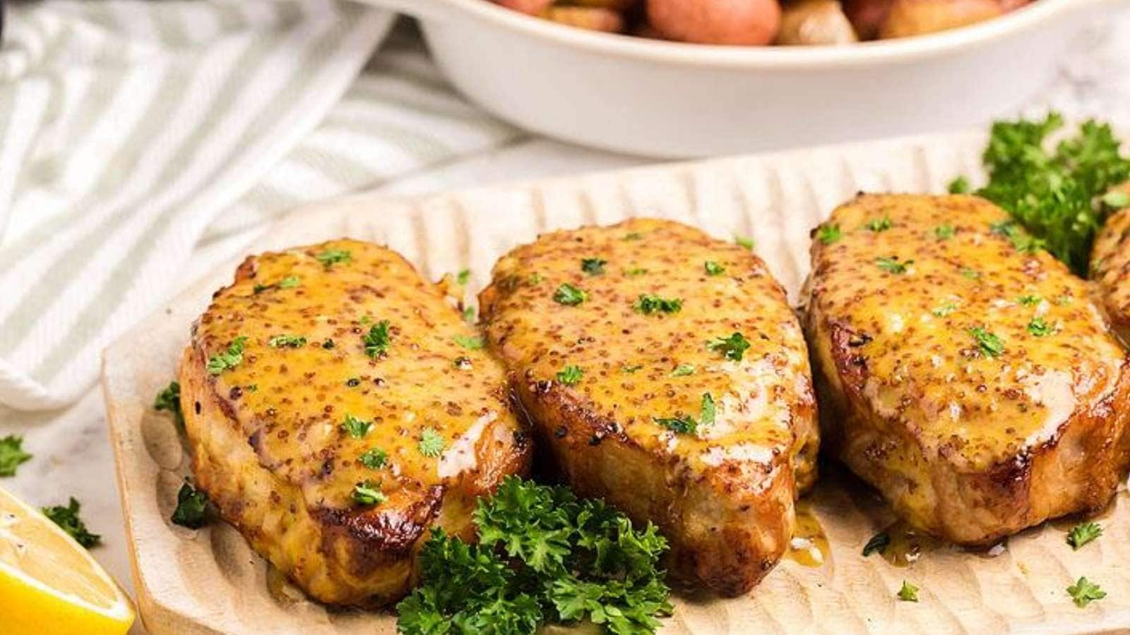 Pork chops on a wooden cutting board with lemon and parsley.