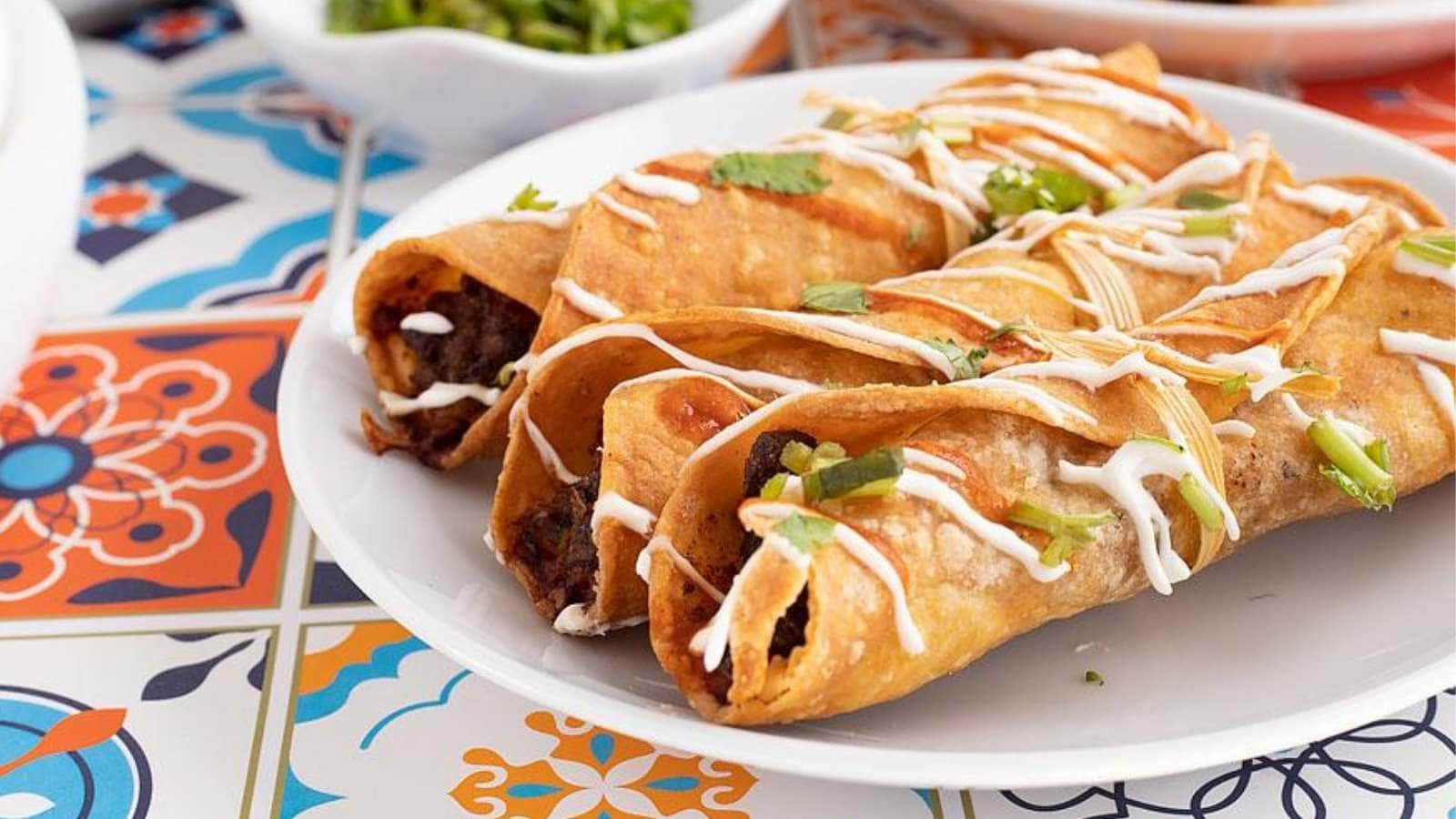 Mexican burritos on a plate with sauce.