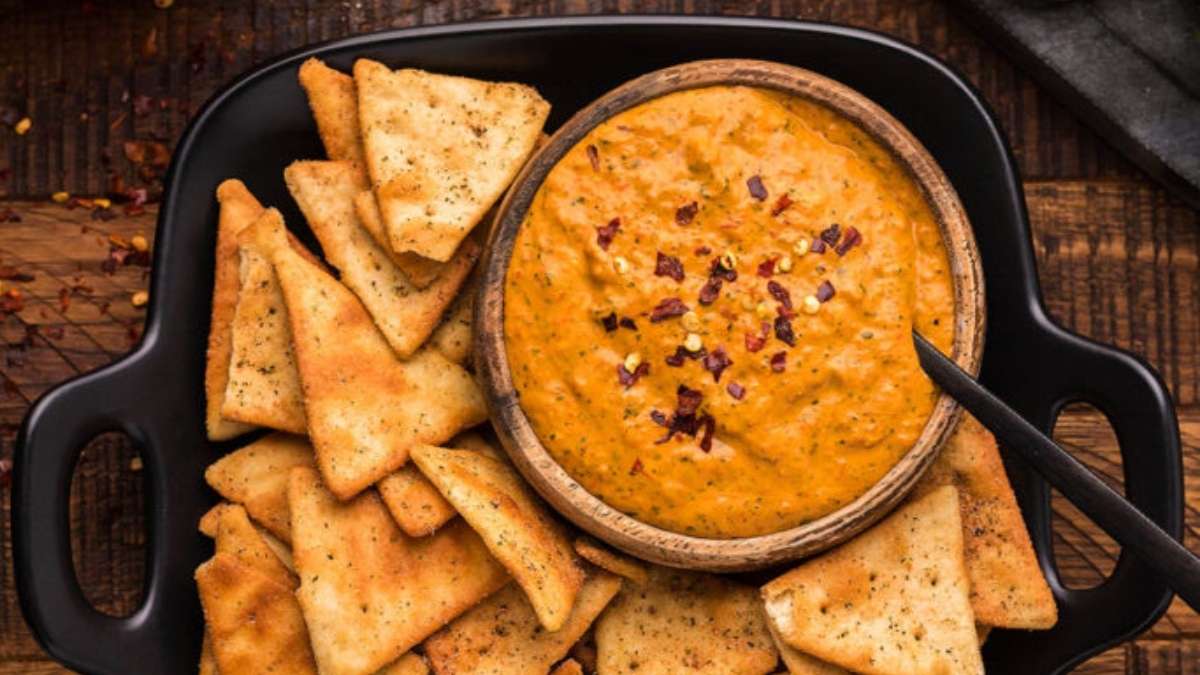 A bowl of pumpkin dip with crackers on a wooden table.