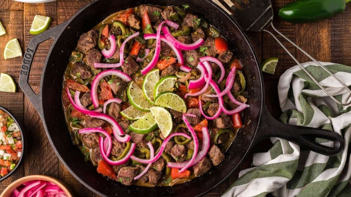 A skillet with beef, onions and peppers on a wooden table.