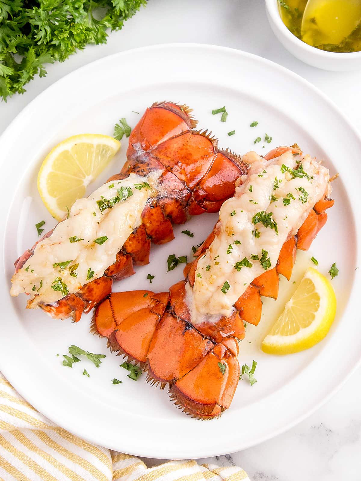 Air Fryer Lobster Tails on a white plate served with lemon wedges.