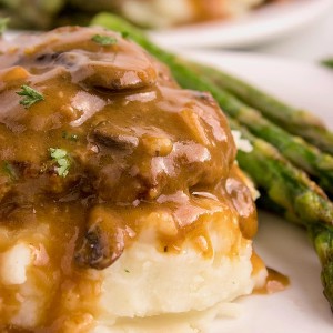 Slow Cooker Salisbury Steak served over mashed potatoes with green asparagus on a white plate.