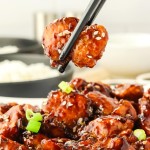 Closeup of a piece of Sesame Chicken held by a chopstick.