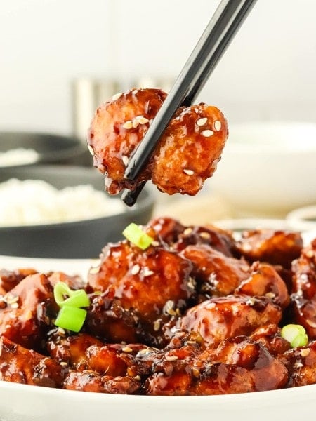 Closeup of a piece of Sesame Chicken held by a chopstick.