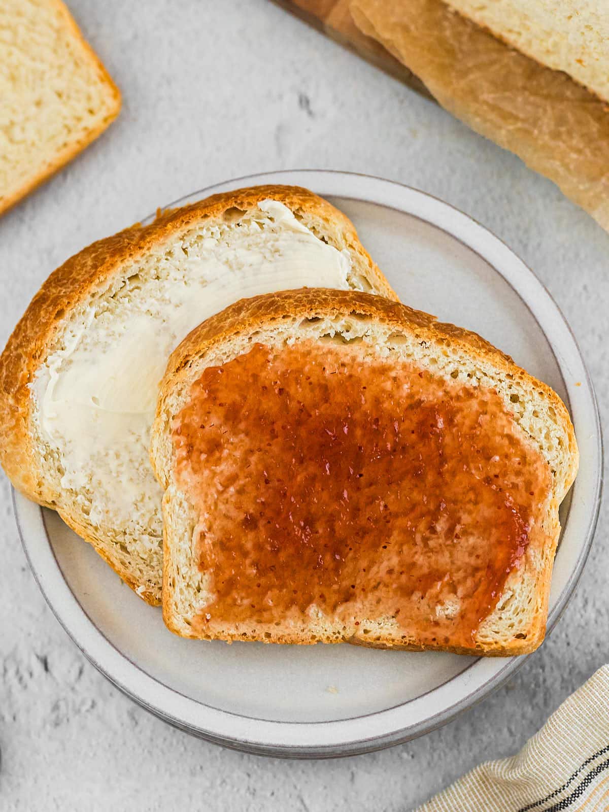 Slice of buttered sourdough sandwich sliced topped with jam.