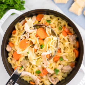 A ladle moving Chicken Noodle Soup from a Dutch oven.