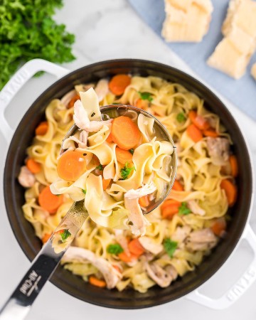 A ladle moving Chicken Noodle Soup from a Dutch oven.
