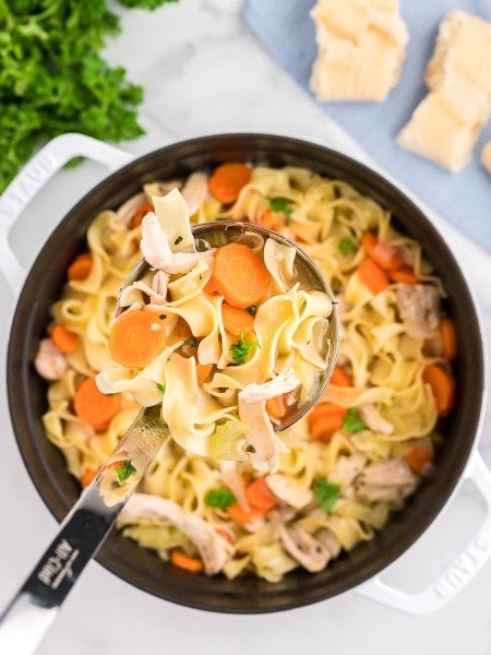A ladle moving Chicken Noodle Soup from a Dutch oven.