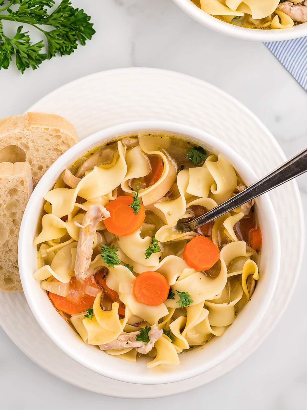 Chicken Noodle Soup in a white bowl served with a slice of bread.