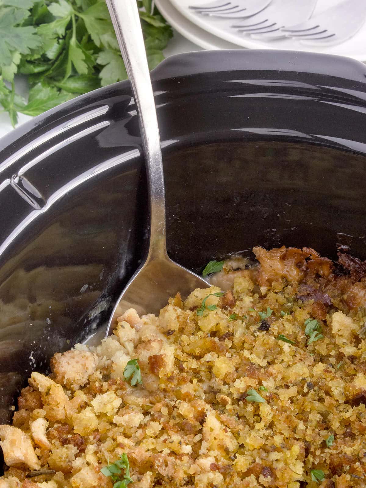 A large serving spoon digging into s slow cooker full of cooked Chicken with stuffing.