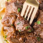 Closeup of a fork stuck into a piece of Steak Bites cooked in an Crockpot.