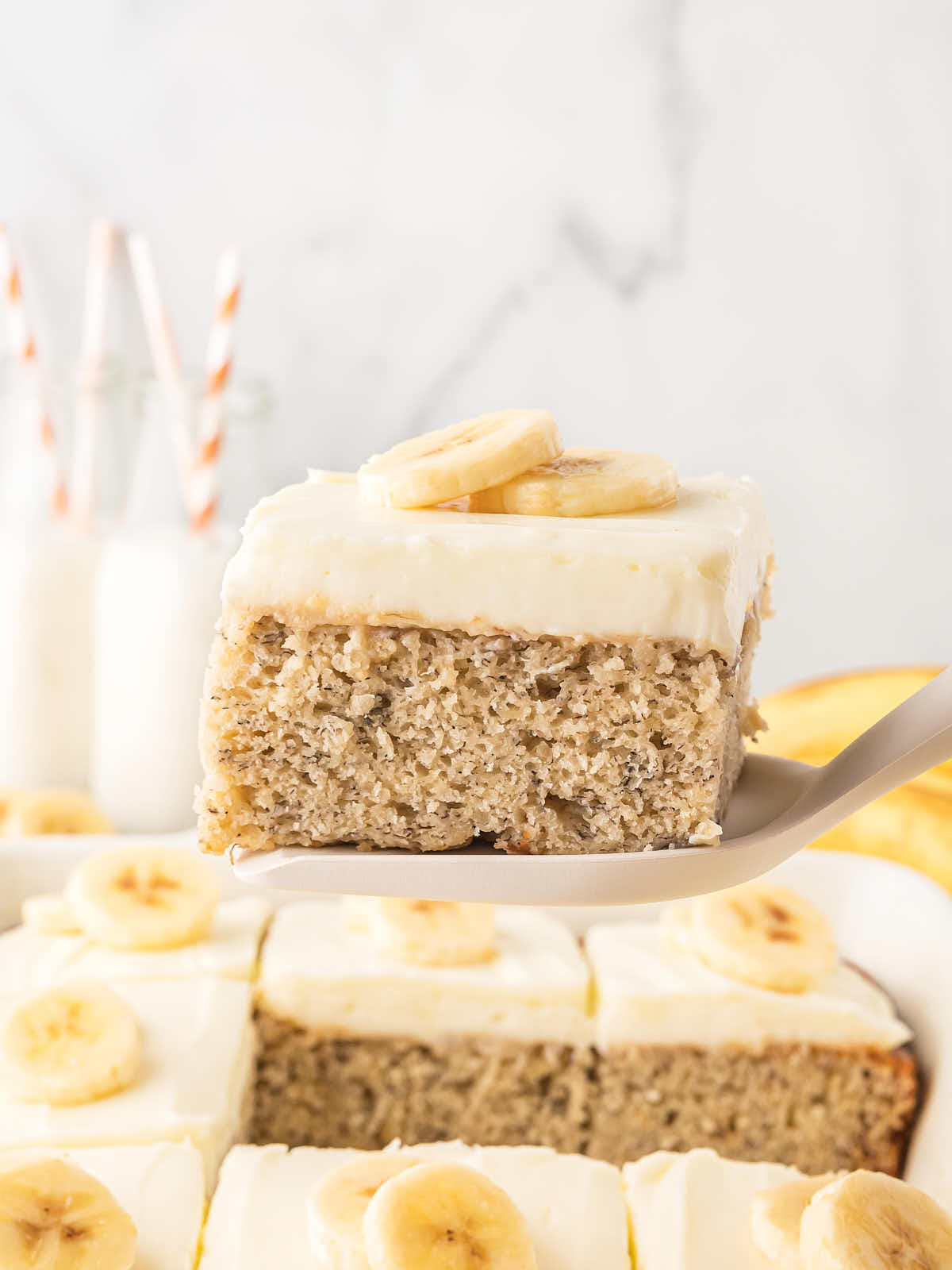 A slice of Banana Cake with Sour Cream Frosting and decorated with banana slices served on a large spoon.
