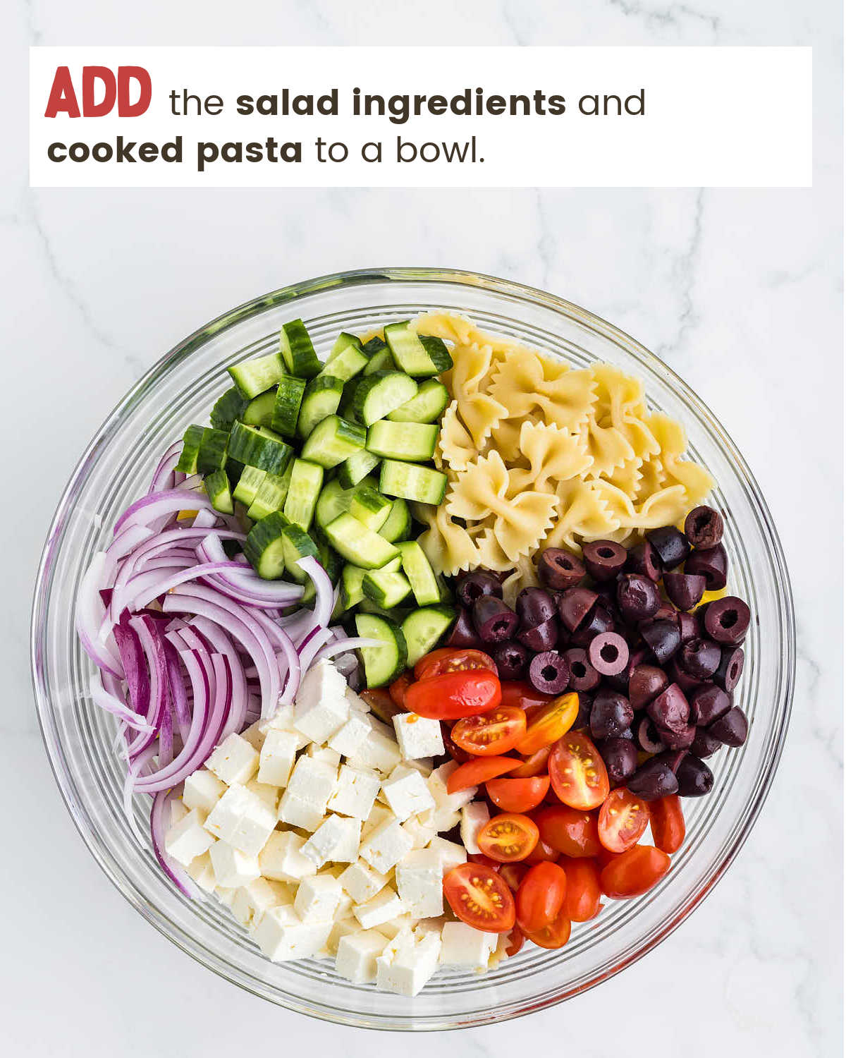 Veggies and pasta in a glass bowl for Greek Pasta Salad.