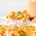 A serving spoon filled with a big scoop of Million Dollar Chicken Casserole.