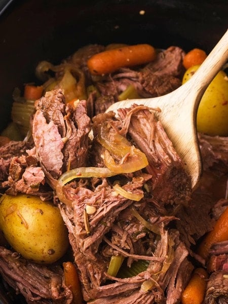 A wooden spoon removing cooked Slow Cooker Sirloin Tip Roast.