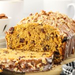 A loaf of Sweet Potato Bread topped with a glazed and drizzled with chopped pecans.