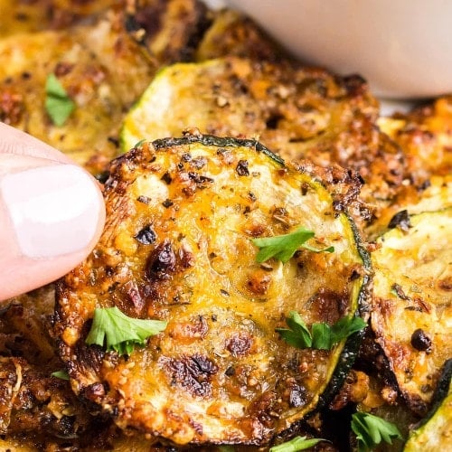 Holding up a slice of air-fried Zucchini Chips.