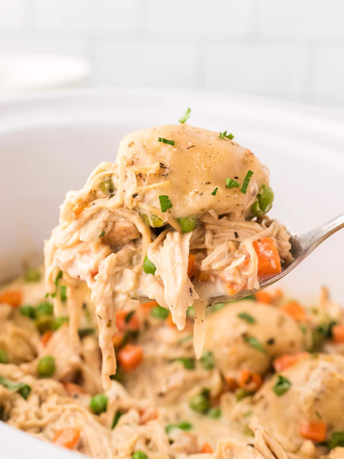 A serving spoon filled with Chicken and Dumplings being removed from a slow cooker.