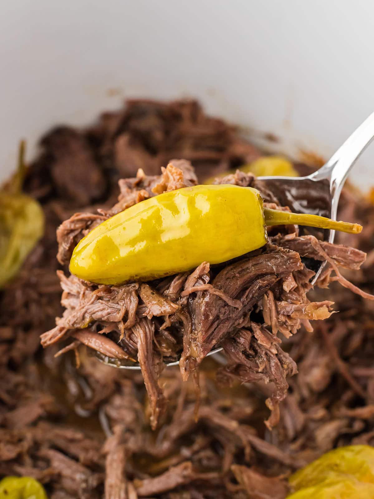 Mississippi Pot Roast on a serving spoon hovering over a slow cooker.