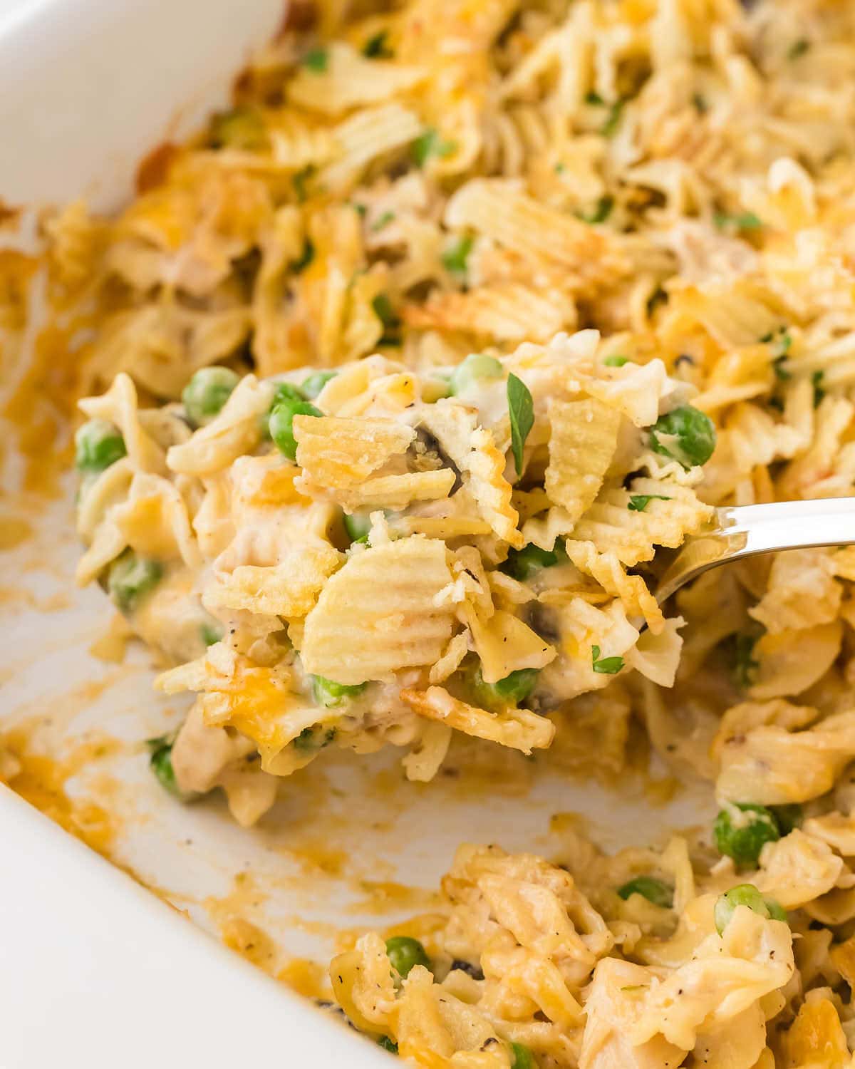 Topdown view of a serving spoon filled with Tuna Noodle Casserole in a white casserole dish.