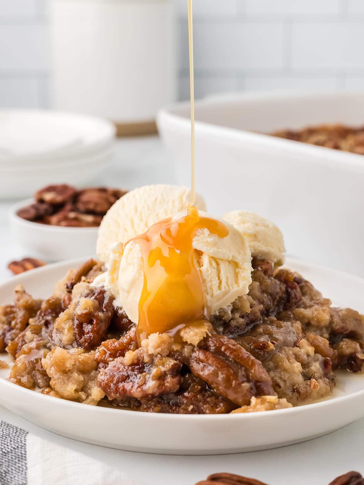 Drizzling salted caramel over Pecan Pie Dump Cake served on a white plate.