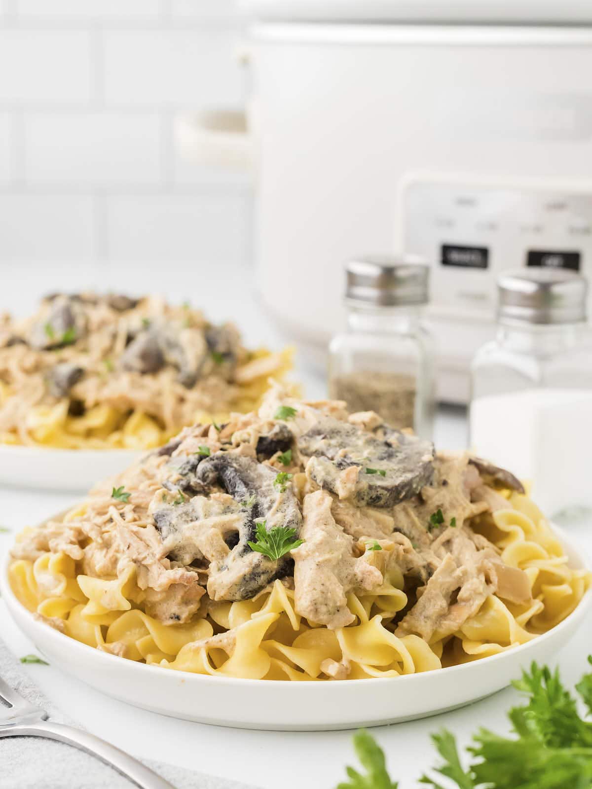 A white plate filled with pasta and topped with Slow Cooker Chicken Stroganoff.