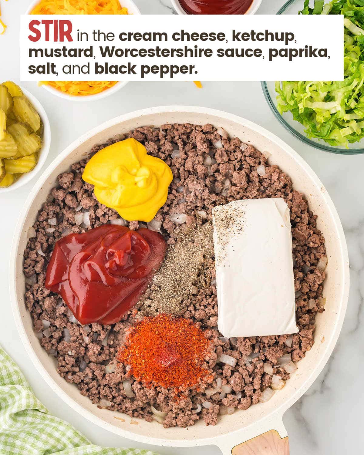 Ground beef, onion, and garlic in a skillet topped with blobs of mustard, ketchup, Worcestershire sauce, cream cheese, and spices.