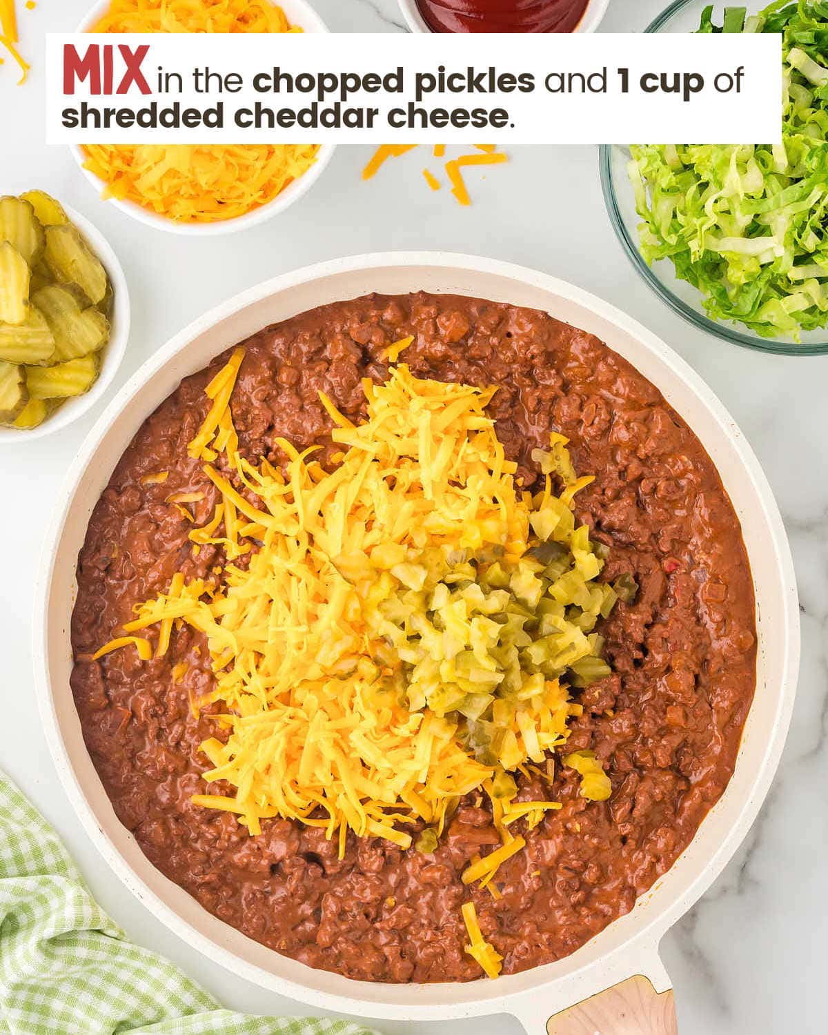 Cooked ground beef mixture in a skillet topped with cheddar cheese and pickle chips.