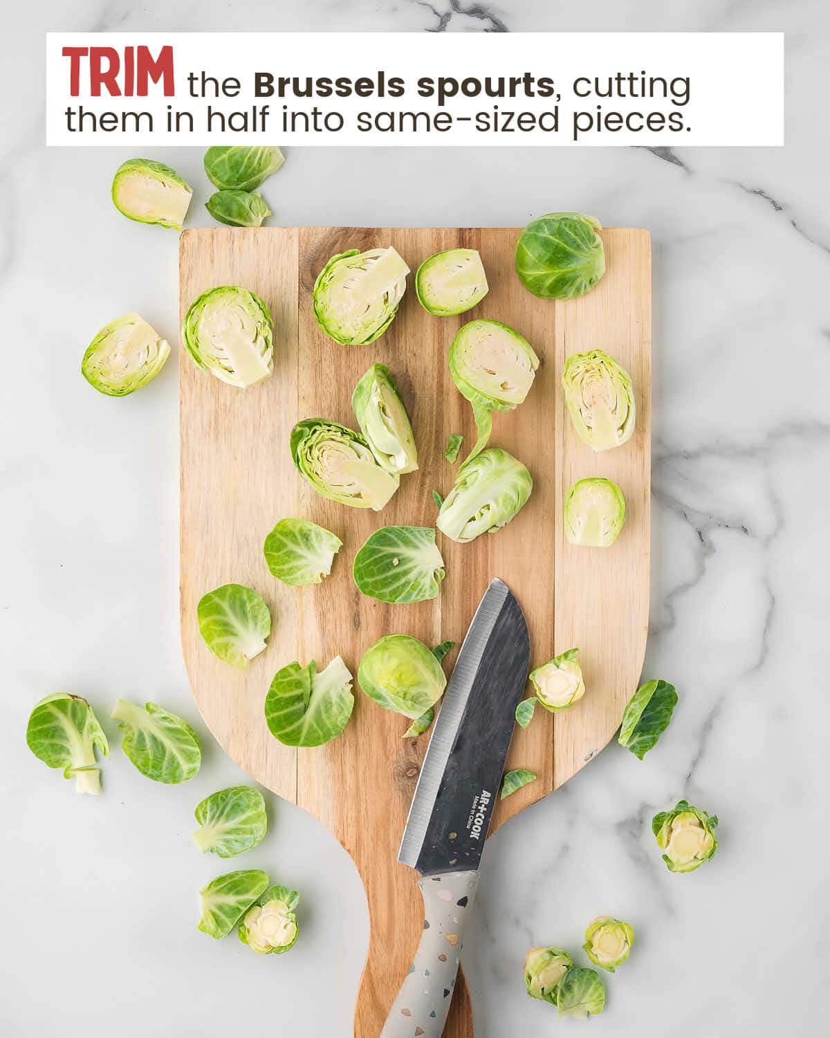 Brussels sprouts on a cutting broad with a knife with text instructions to cut them in half. 