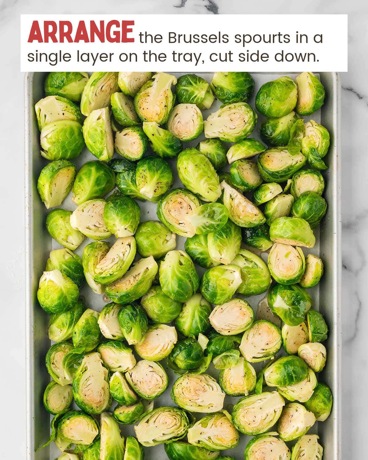 Brussels sprouts are on a baking tray with text instructions on how to arrange them in a single layer.