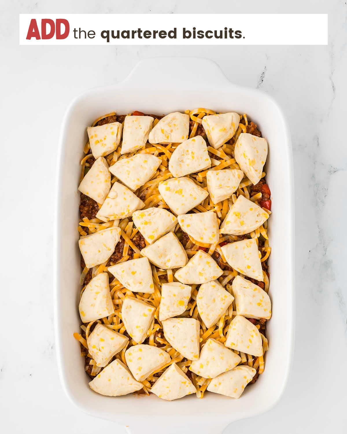 Quartered biscuits on top of meat and cheese as a step in making sloppy joe casserole.