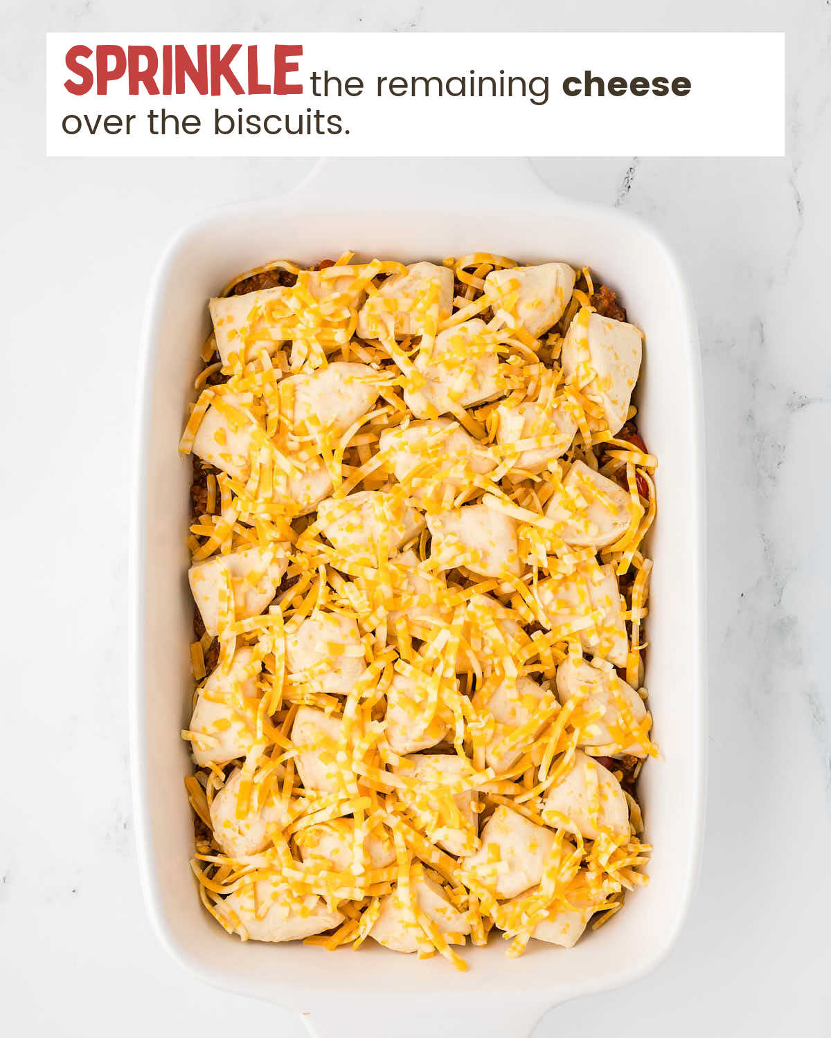 Cheese on top of biscuits as a step in making sloppy joe casserole.