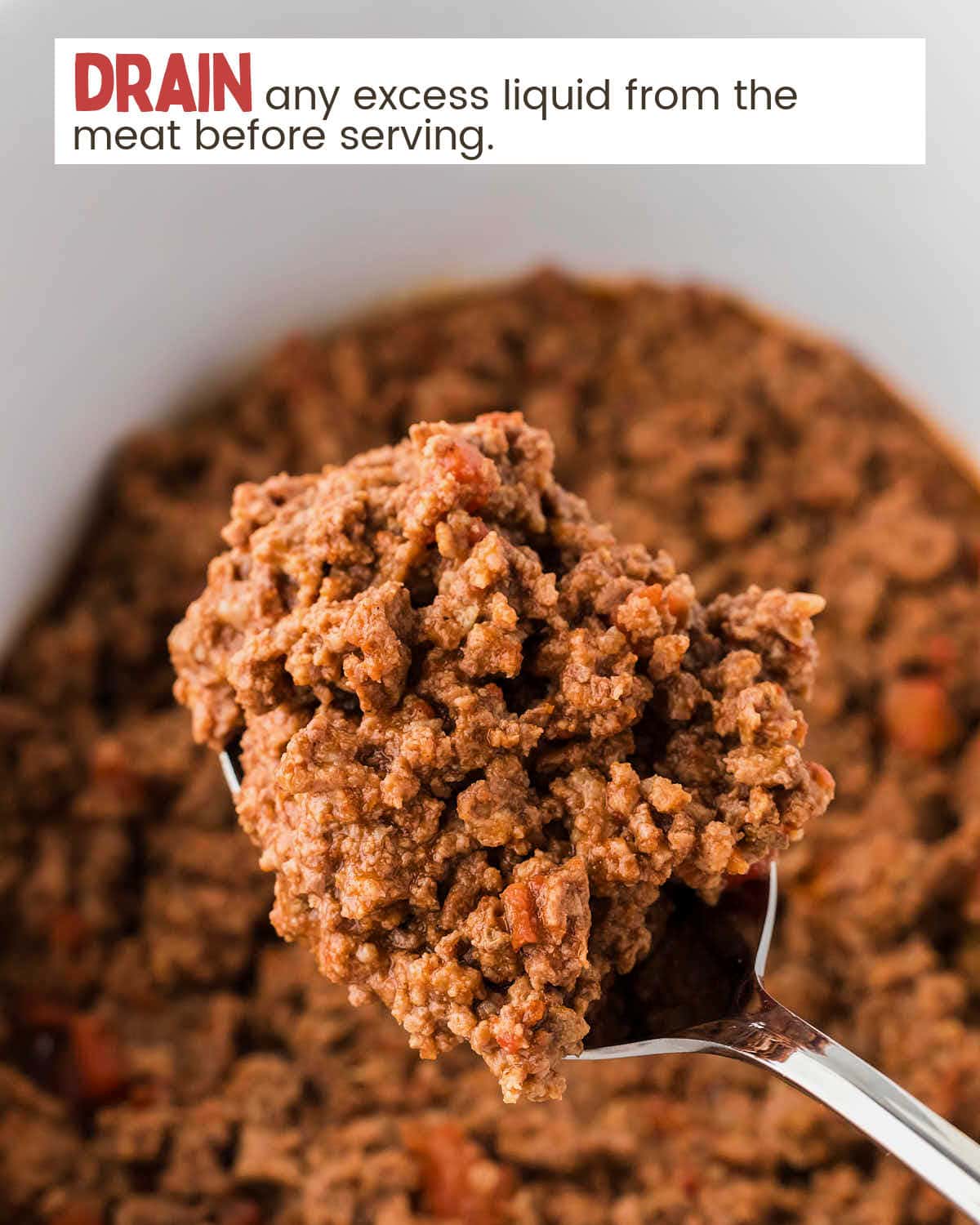 A top-down view of a slow cooker with a spoon lifting a scoop of cooked taco meat.
