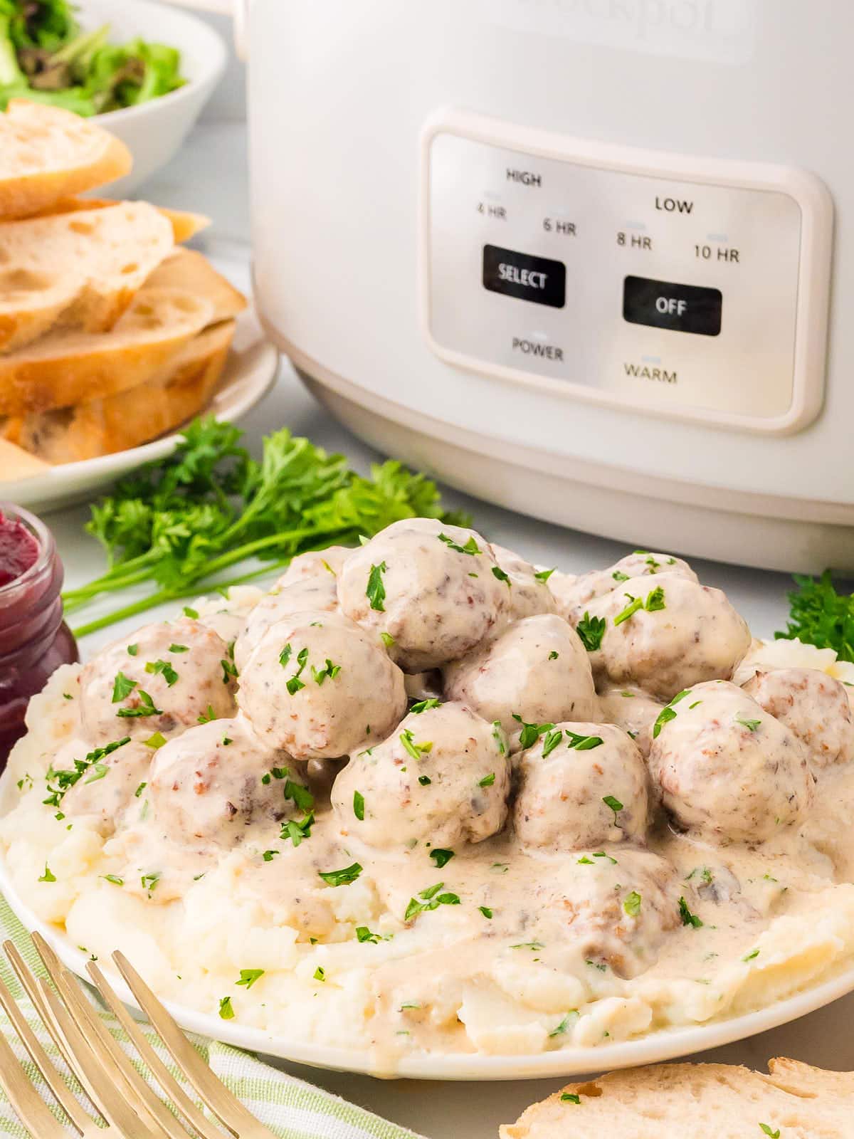 A plate of Slow Cooker Swedish Meatballs and mashed potatoes next to a Crock Pot.