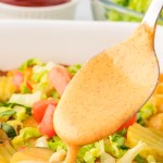 Closeup of a spoon dripping homemade Big Mac Sauce over a casserole dish.