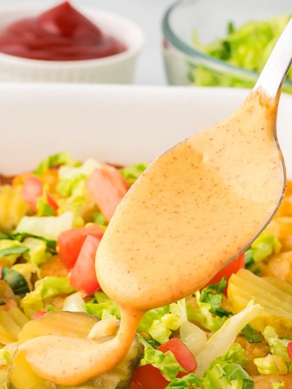 Closeup of a spoon dripping homemade Big Mac Sauce over a casserole dish.