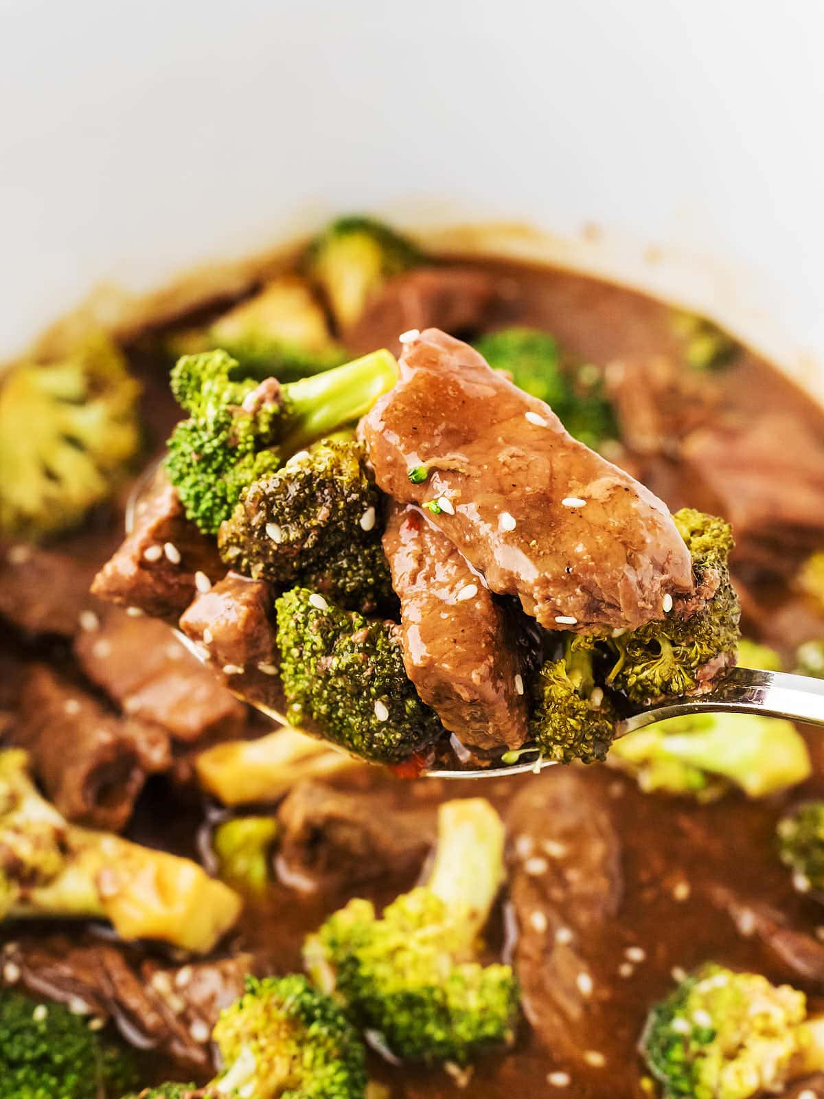 A serving spoon ladling cooked Beef and Broccoli out of a Crockpot.