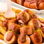 German Currywurst served with French fries in a white bowl.