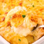 A serving spoon full of freshly baked Scalloped Potatoes taken from a casserole dish.