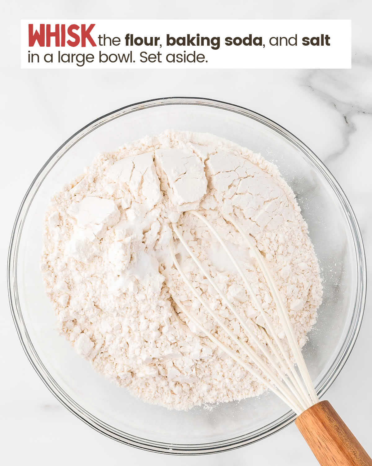 Dry ingredients for chocolate chip cookies in a bowl with a whisk.