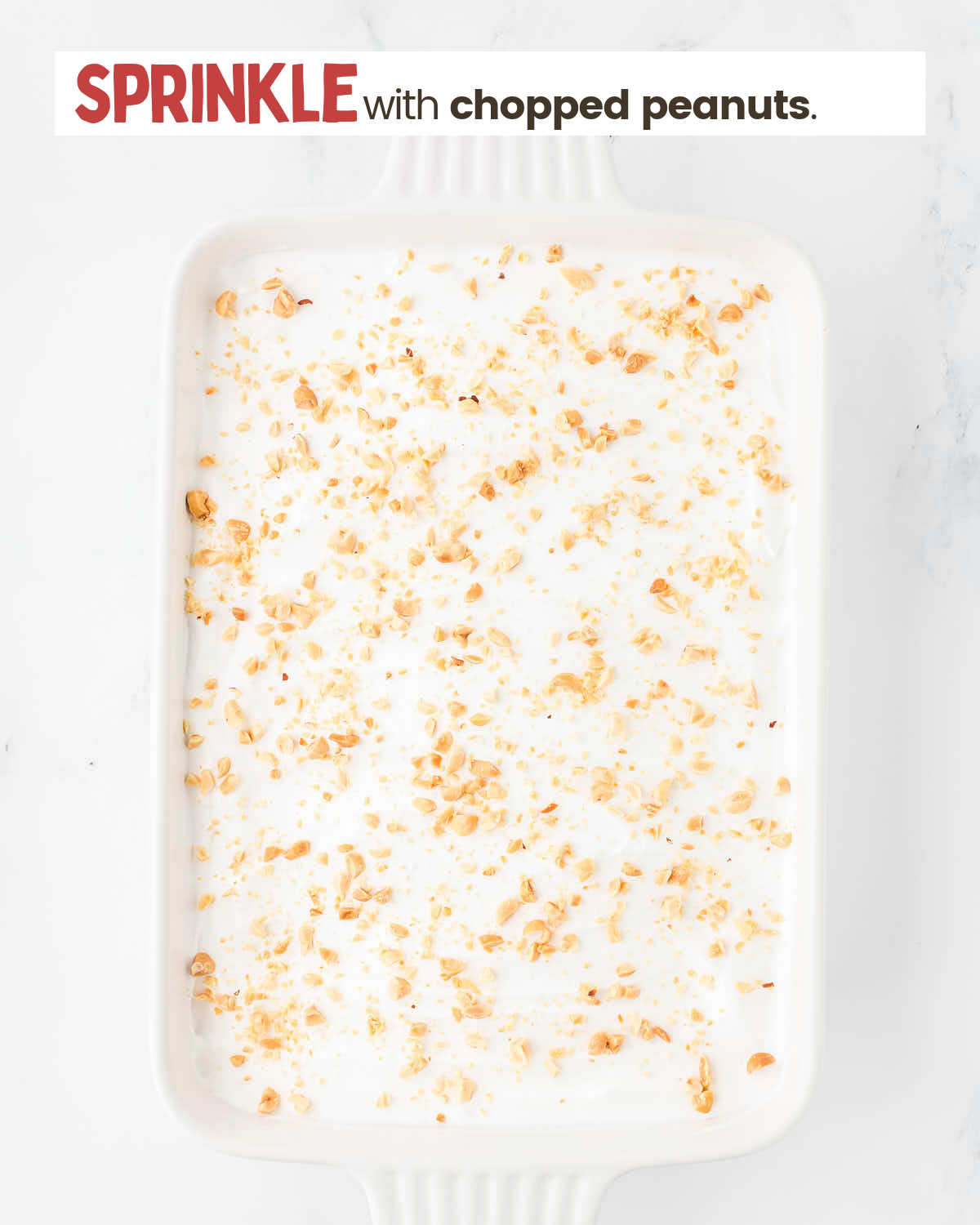 Whipped topping layer in a baking dish covered with chopped peanuts.