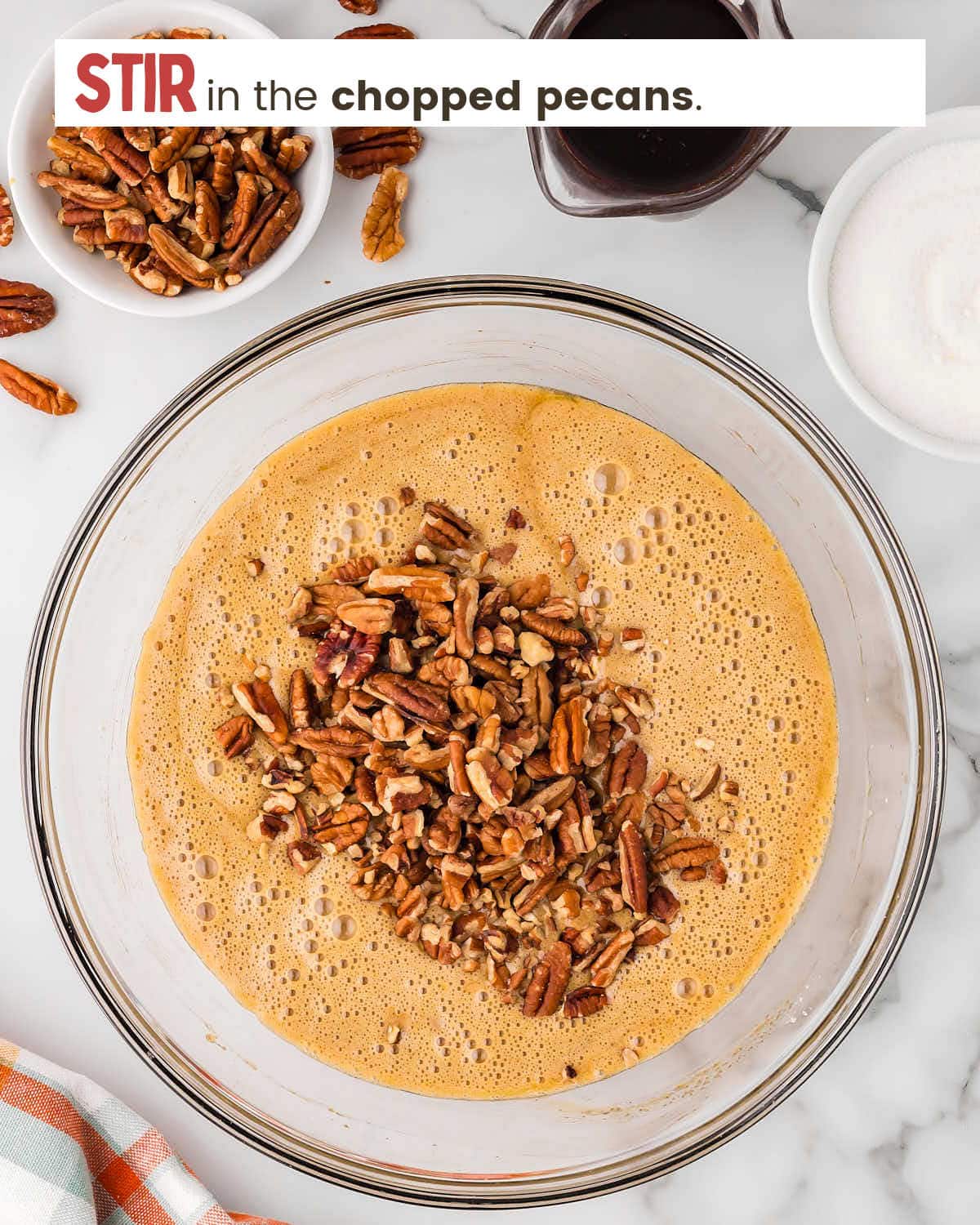 Pecan pie filling ingredients in a mixing bowl with chopped pecans on top.